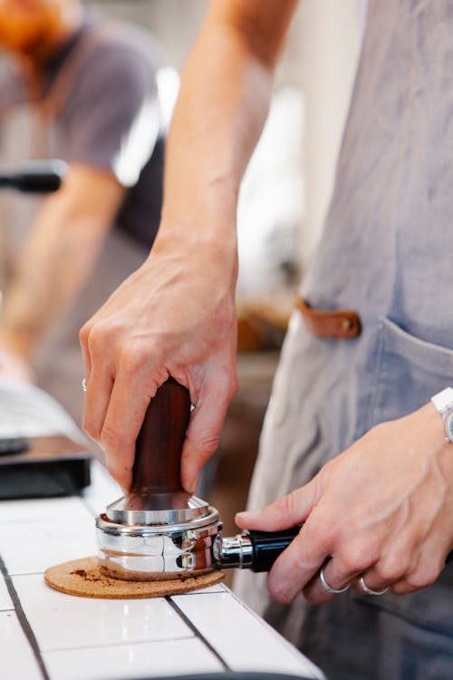 Faceless barista tamping coffee in portafilter in cafe kitchen