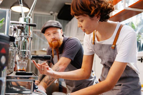 Crop baristas talking while brewing coffee in professional machine