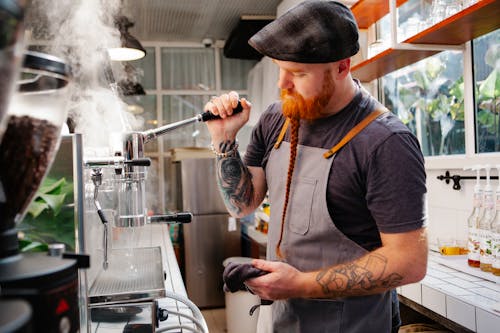 Tattooed barista cleaning coffee maker with steam