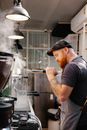 Side view of masculine male worker touching lever of coffee maker with vapor during cleaning process in cafeteria