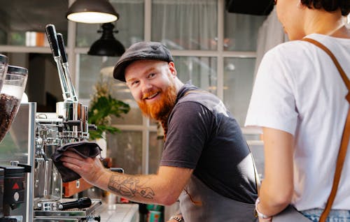 Cheerful barista speaking with crop coworker against coffee machine