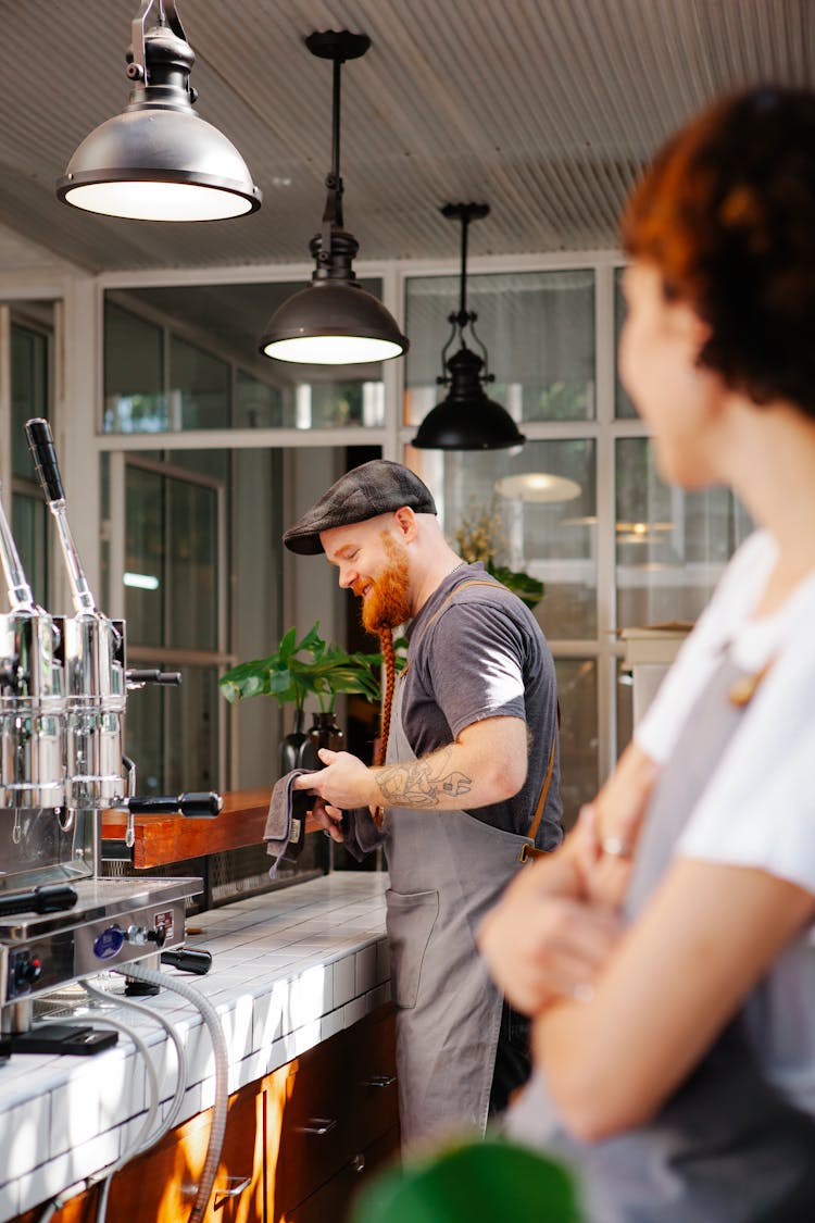 Hipster Barista Speaking With Anonymous Colleague Against Coffee Maker Indoors