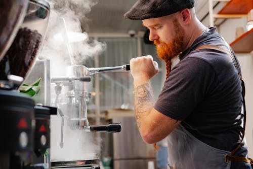 Crop employee cleaning espresso maker with vapor at work