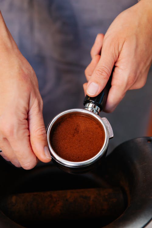 High angle of crop anonymous female cafe employee showing metal portafilter with tamped coffee