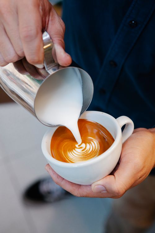 Free From above of crop unrecognizable male employee pouring milk from jug into tasty coffee with froth in cafe Stock Photo