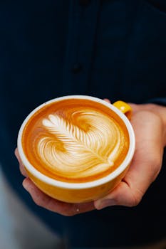 Artistic latte with leaf pattern in a yellow cup, symbolizing coffee culture.