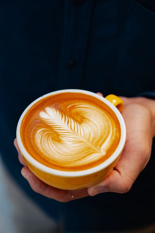 Free High angle of crop anonymous cafeteria employee with ceramic cup of delicious coffee with ornament on froth Stock Photo