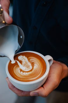 Close-up of barista pouring milk for latte art in a coffee cup.