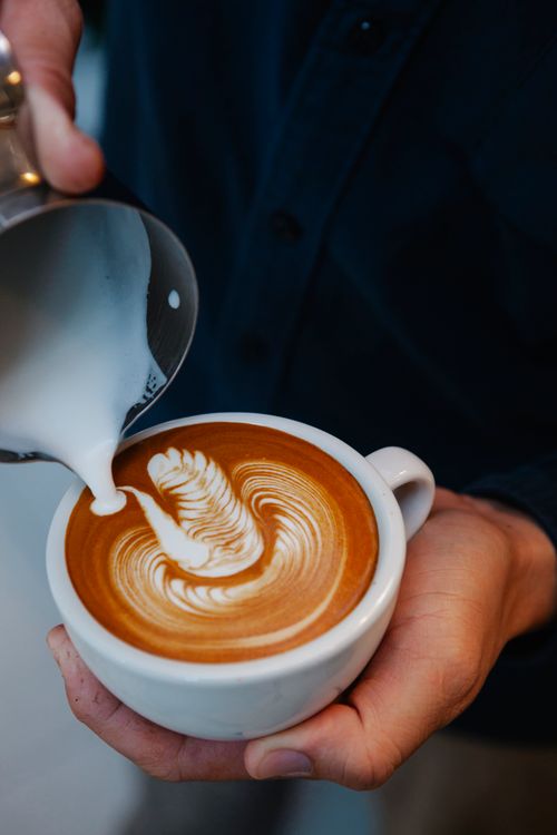 Free From above crop anonymous male barista pouring frothy milk into coffee cup and making latte art while working in cafe Stock Photo