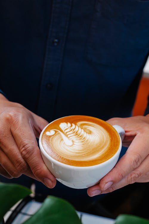 Free From above crop anonymous male barista serving cup of delicious freshly brewed latte with art in cafeteria Stock Photo