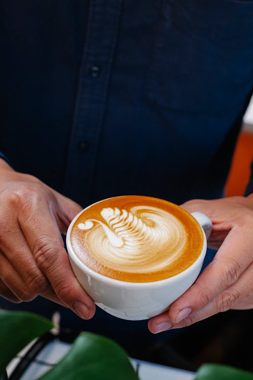 From above crop anonymous male barista serving cup of delicious freshly brewed latte with art in cafeteria