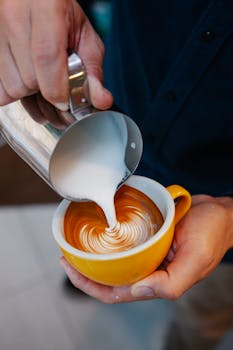 From above of crop anonymous bartender making tasty coffee with latte art while pouring cream into mug