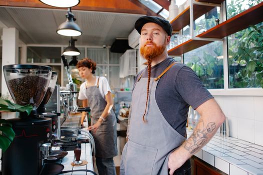 Barista with red beard with pigtail and tattoo