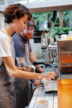 Side view of man and woman in aprons making tasty aromatic coffee with metal coffee machine in kitchen of cafe