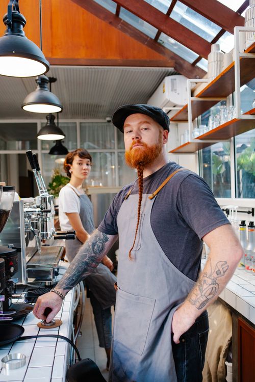 Free Young creative hipster man and woman in aprons standing in modern cafe with lamps and coffee machines Stock Photo