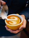 From above of crop anonymous male pouring cream into mug with coffee while making latte art