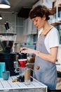 Side view of female barista in apron pouring water into coffee dripping through paper filter in cafe
