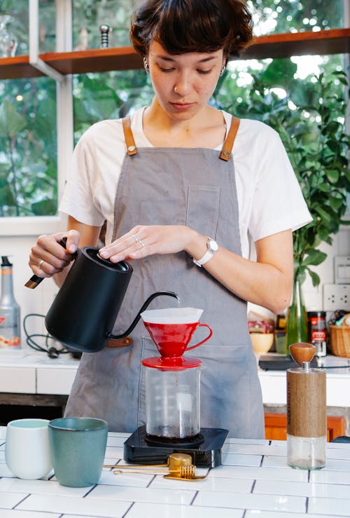 Free Pensive female barista pouring coffee in light kitchen Stock Photo