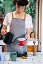 Crop female barista in gray apron standing at table and preparing coffee in alternative way in cafe in daytime