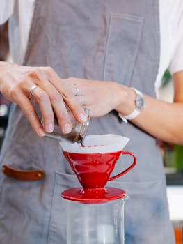 Close-up of a barista pouring coffee grounds for a pour-over in a café setting.