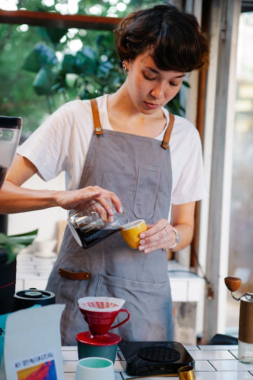 Woman pouring fresh aromatic coffee from jug into cup