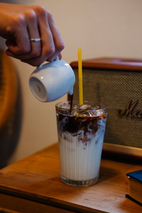 Crop anonymous female making chocolate milky cocktail in glass on wooden counter in cafe