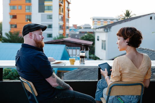 Back view of young woman with tablet and stylish man resting with cup of coffee in terrace in daytime