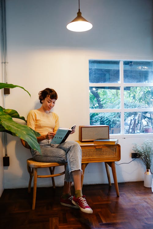 Young woman reading book on chair under bright lamp