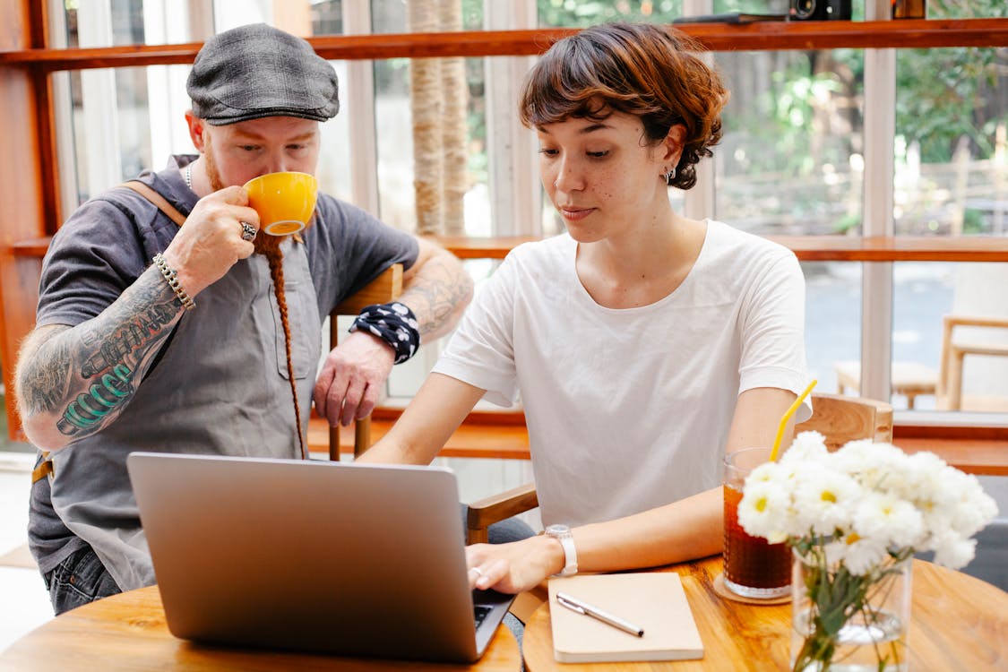 Free Pensive young woman typing on netbook while man with cup drinking coffee at table of cafe Stock Photo