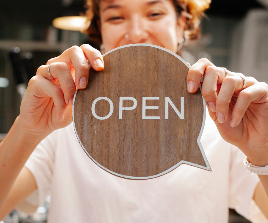 Free Happy woman showing wooden signboard saying open Stock Photo