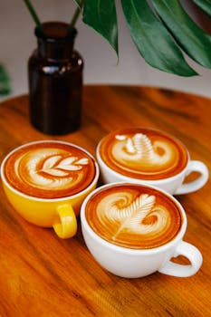 Captivating latte art in vibrant coffee cups on a wooden café table, showcasing café culture.