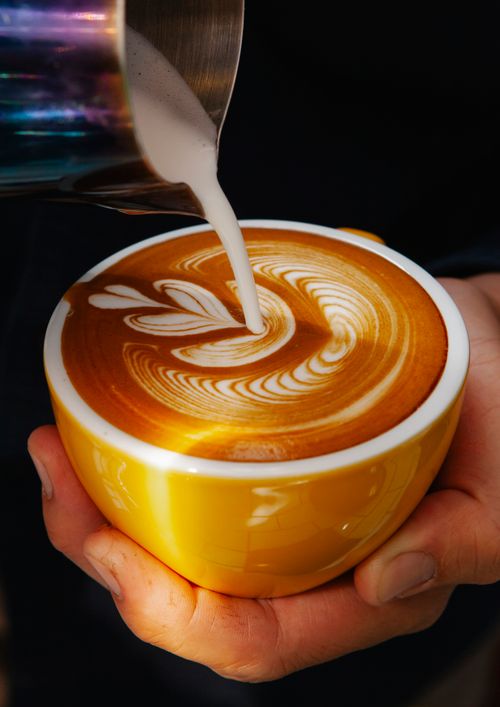 Free Unrecognizable professional male barista with mug of coffee making latte art with leaf pattern in modern coffee house during work Stock Photo
