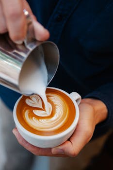 Close-up of a barista pouring milk into a latte, creating a heart latte art design.