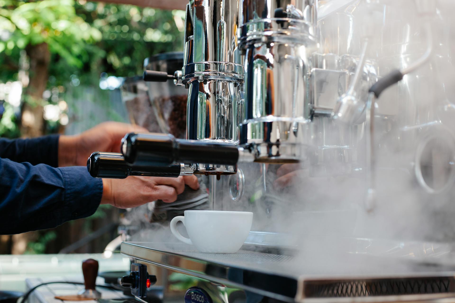 Unrecognizable professional barista working on coffee machine with steam while making coffee on street against blurred background during work process