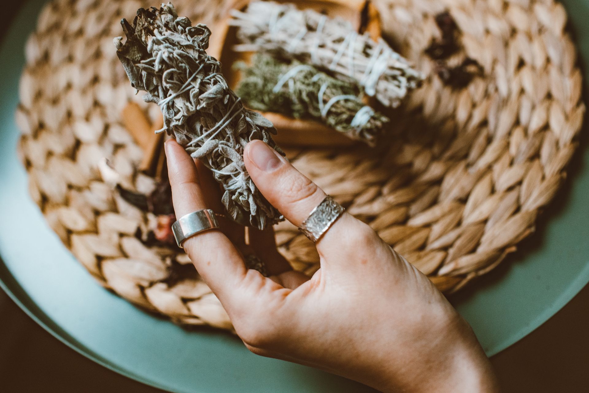 A hand holding a sage smudge stick over a woven mat, evoking a calming ritual ambiance.