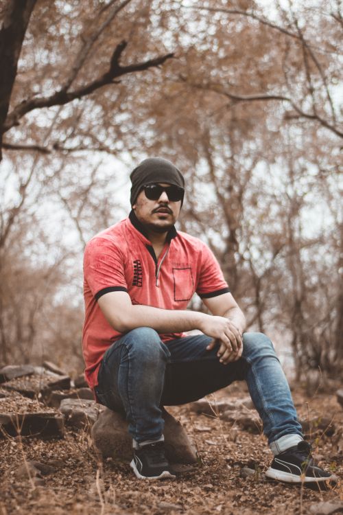 Free A man wearing sunglasses and a casual outfit sitting on a rock in a serene autumn forest setting. Stock Photo