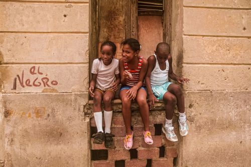 Free Three children sitting on a window sill in Havana, Cuba, laughing and enjoying a sunny day. Stock Photo