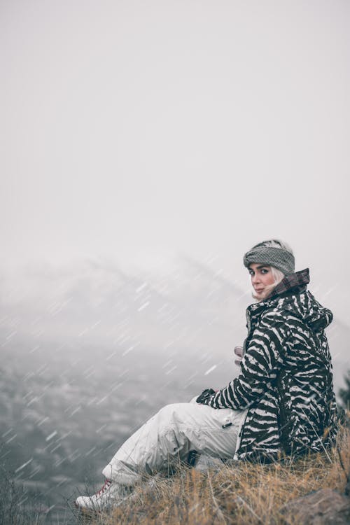 A Woman in Printed Jacket Sitting on the Field while Snowing