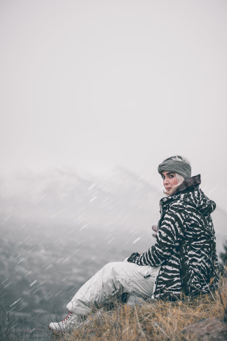 A Woman In Printed Jacket Sitting On The Field While Snowing