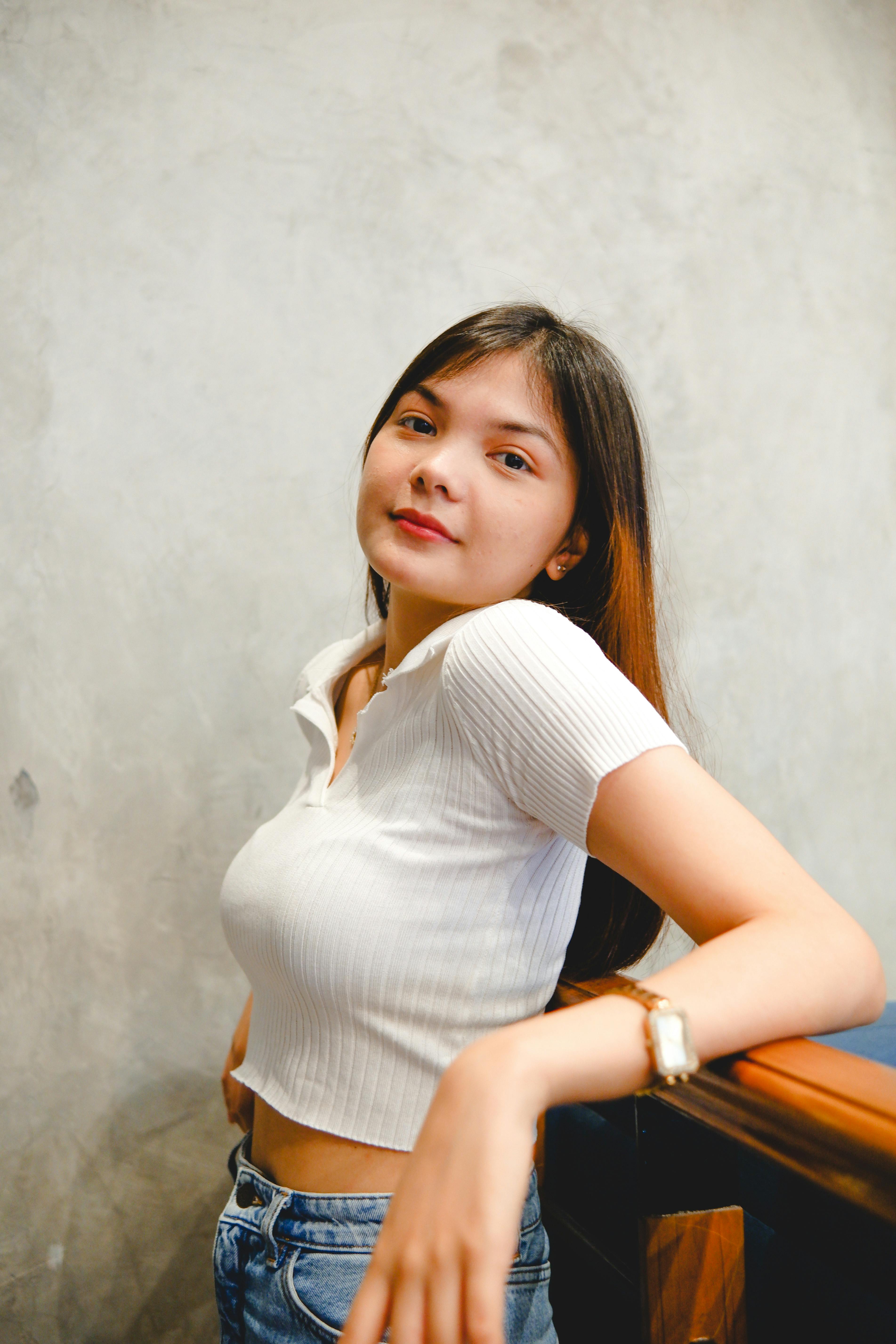Smiling brunette woman in casual white top posing indoors, leaning on railing.
