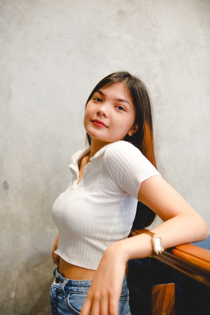 Smiling brunette woman in casual white top posing indoors, leaning on railing.