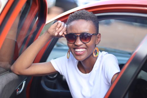 Free A joyful woman wearing sunglasses and a white t-shirt smiles while sitting in a car. Stock Photo