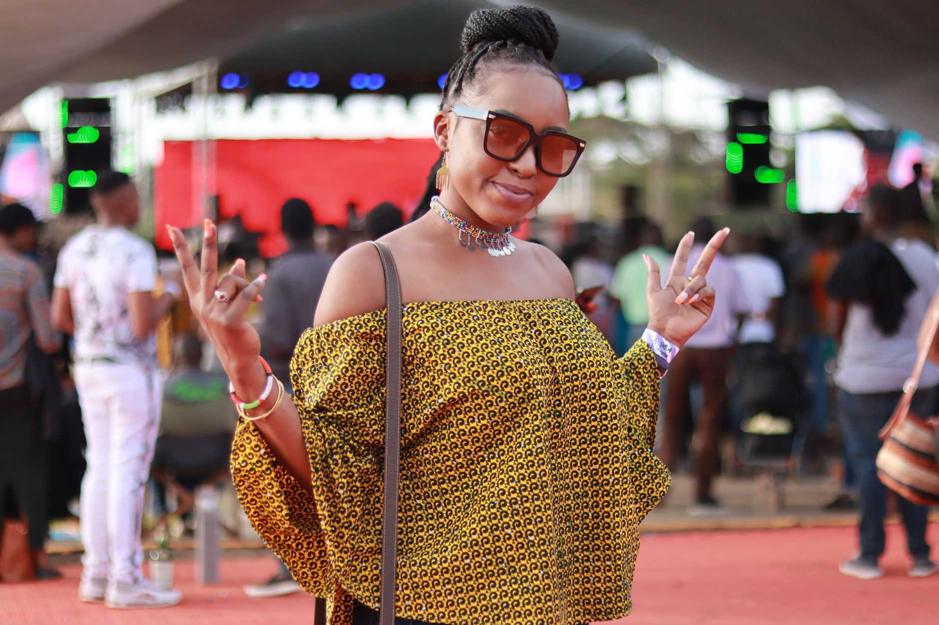 Woman posing with peace signs at an outdoor concert, showcasing style and enjoyment.