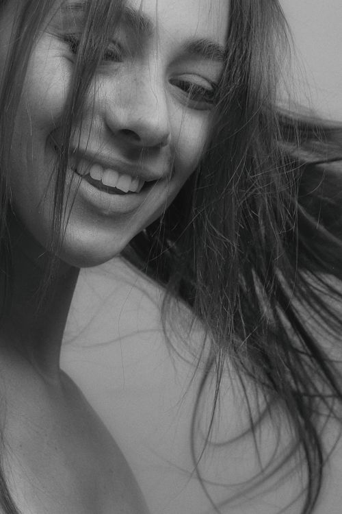 Free Close-up black and white portrait of a smiling woman with tousled long hair, exuding playfulness. Stock Photo