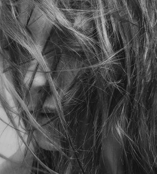 Intimate black and white close-up of a woman's face partially hidden by windblown hair, capturing mystery and emotion.