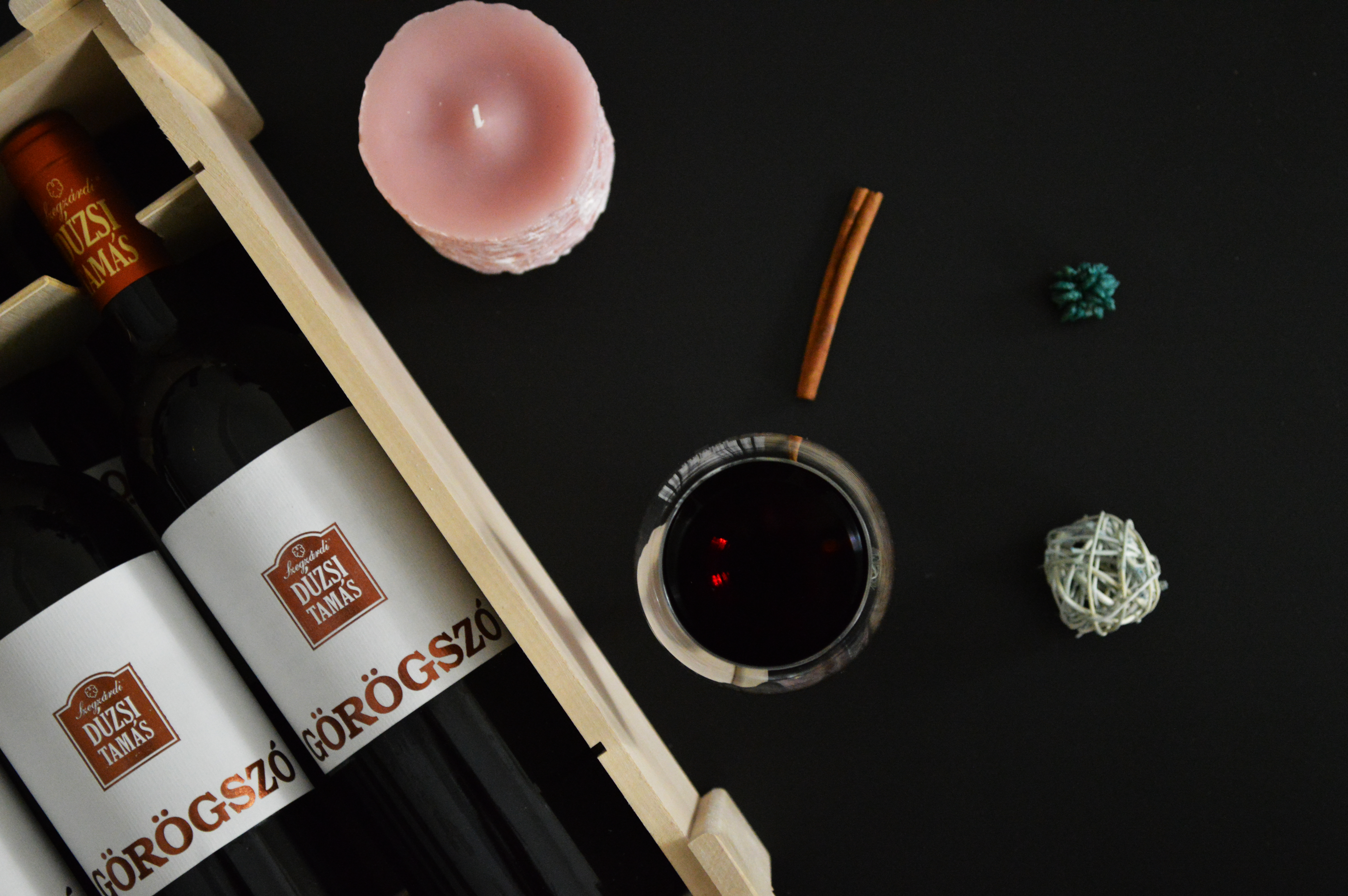 Flat lay of red wine bottles with a candle and cinnamon stick on a dark background.