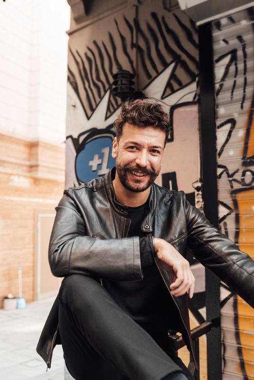 Free Confident cheerful male with mustache and beard standing with leg raised on street against vandalized wall and looking at camera with smile Stock Photo