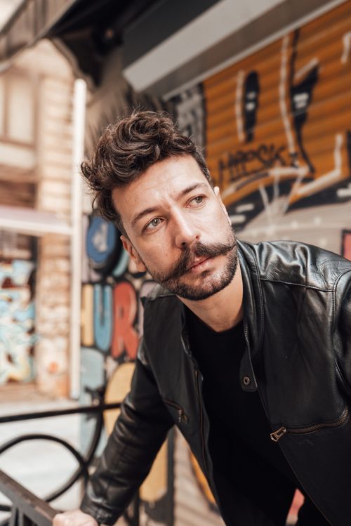 Free Pondering adult male with mustache and beard in leather jacket standing on street with graffiti on wall and looking away in thoughts Stock Photo