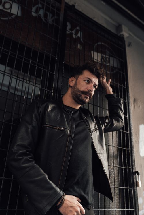 Free Confident serious male with mustache and beard standing with arm raised against grid wall and looking away pensively Stock Photo