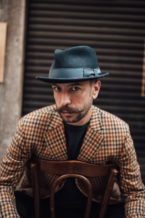 Attentive stylish man sitting on chair outside building wall